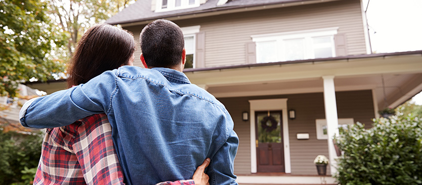 Couple standing in front of a home embracing and looking toward it