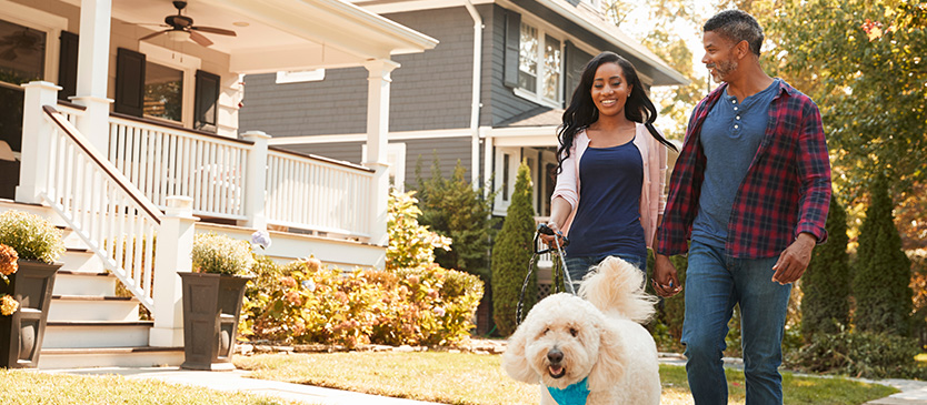 two people walking their dog in a neighborhood and smiling